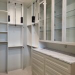 Finished walk-in closet with painted white cabinetry, glass-front uppers, marble countertop, and pull-down hanging rods installed.