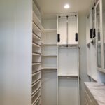 Finished walk-in closet with face-frame shelving, dual hanging rods with black pulls, and adjustable shelves—fully painted white.