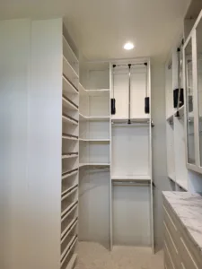 White painted closet shelving with pull-down hanging rods and marble countertop, fully finished.