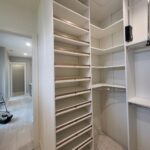 Installed white face-frame closet shelving with adjustable brackets and wood support cleats throughout walk-in closet.
