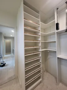 White finished closet shelving tower with many thin shelves in the corner, hallway visible through doorway.
