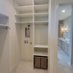 Custom built-in closet shelving with painted white face-frame cabinetry, multiple cubbies, and lower bench storage with fabric bins.