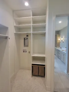 White built-in closet shelving with cubbies and a hanging rod, bathroom visible through doorway.