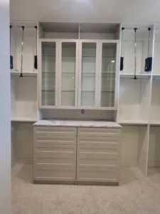 Cabinetry with white glass front doors, marble countertop, and chrome closet rods installed