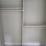 Closet shelving and hanging rods installed with raw wood rods on white metal brackets, ready for paint.