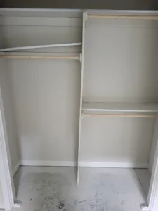 Closet hanging rods installed in a crossed pattern, painted walls, concrete floor still unfinished.