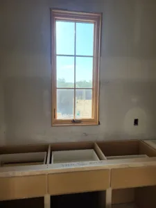 Tall window casing installed with mitered corners over an unfinished cabinet base, raw wood