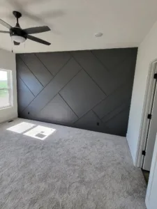 Chevron pattern accent wall painted dark gray, fully finished with carpet flooring and a ceiling fan