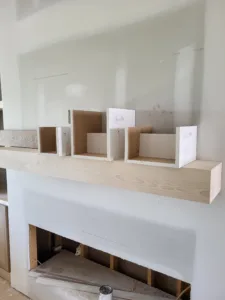 Raw wood mantel beam installed above a framed fireplace opening, with cubby box mockups staged on top