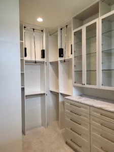 Finished closet cabinetry with glass front upper doors, drawer bank hardware, and hanging rods