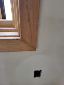 Wood window casing corner, with a small drywall access hole nearby