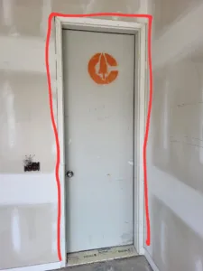 Primed white flush door set in a drywalled opening, casing not yet installed, red layout marks on the wall.
