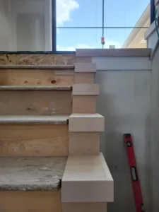 Stacked wood blocking at a stair stringer end beside a window, framing stage for a false tread cap.