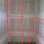 Closet layout marked with red tape showing planned shelf and rod placement before installation.