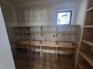 Raw lumber shelf framework under construction in closet, small window visible, framing stage.