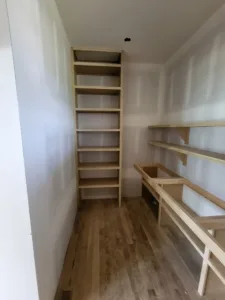 Narrow closet under construction with a raw wood shelf ladder along one wall, hardwood floor visible.