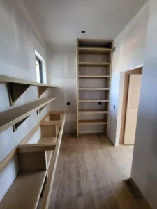Raw wood shelving following a sloped ceiling with a tall vertical shelf tower, hardwood floor visible.