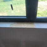 Raw wood window sill installed, pre-paint, with construction dust visible on surface.