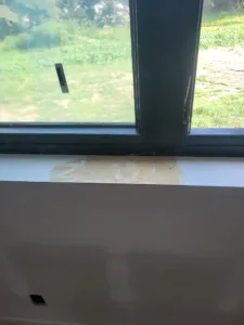 Unpainted wood window sill with visible wood filler, set below a dark-framed window facing a field