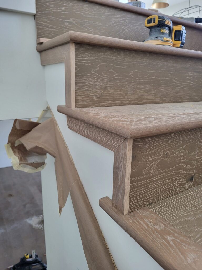 Stair skirt board and oak treads mid-install with a sander on the tread