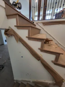 Stained wood stair treads with mitered end returns, protective paper taped along the stringer