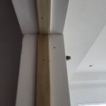 Installed door jamb or casing edge with visible nail holes and raw wood finish between drywall surfaces.