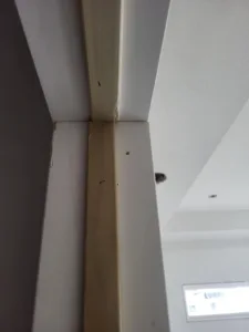 Raw wood corner trim installed at a ceiling angle change, nail holes visible, unfinished