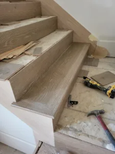 Oak stair tread with mitered nosing installed over primed riser, construction tools on floor below