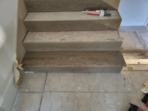 Three unfinished oak stair treads and risers installed against subfloor, ready for paint