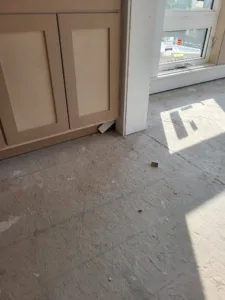 Unfinished cabinet doors installed near a window opening on a bare subfloor during construction