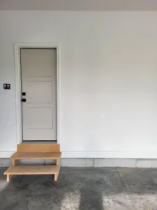 Painted white single exterior door with wood step platform leading up to threshold, completed