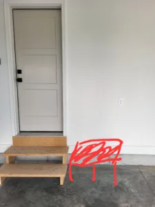 Painted white single exterior door with black hardware and wood step platform below threshold, completed