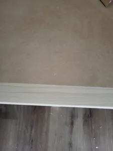 Light wood baseboard installed over dark wood-look flooring, grain visible in the trim.
