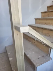 Closeup of a wood handrail with a mitered corner joint on an unfinished plywood stair stringer