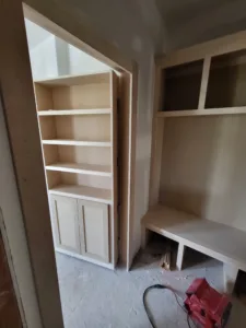 Built-in shelving alcove with open shelves above and lower cabinet doors, raw wood ready for paint