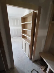 Built-in bookcase with open shelves above and closed cabinet doors below, unfinished raw wood