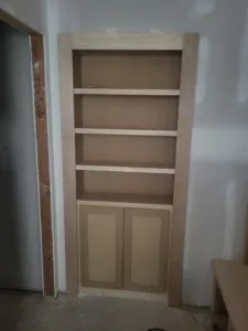 Built-in bookcase with four open shelves and lower cabinet doors, raw wood ready for paint