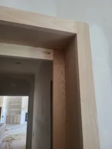 Raw wood door trim corner with a mitered joint, unfinished, seen through an interior doorway