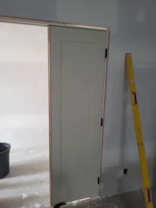 Door slab hung on black hinges within the jamb, level leaning nearby, drywall stage visible.