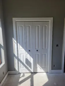 Painted white closet doors with raised panels, closed, natural light casting shadow across them.