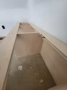 Raw plywood built-in frame with angled supports in a corner, unfinished construction stage
