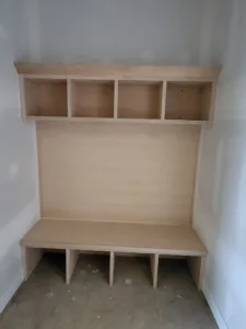 Built-in mudroom locker with four open upper cubbies and four lower cubbies, raw unfinished plywood.