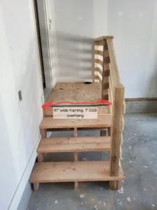 Garage steps with three open treads and a slat rail leading up to an OSB landing at the house door, mid build