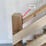 Fluted wood newel post installed at stair opening with raw wood treads and drywall surround.