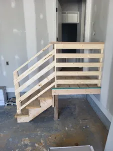 Horizontal wood slat railing installed on a small unfinished stair platform