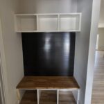 Built-in shelving unit with white face-frame cubbies, dark shiplap backing, and wood countertop surface.
