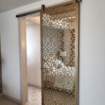 Finished barn door with decorative metal scrollwork panel hung on overhead track with hardware installed.
