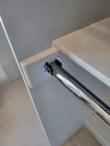 Chrome closet rod mounted on a wall bracket beneath a shelf, installed above carpet flooring.