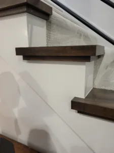 Dark stained floating shelves mounted on white wall beside a staircase, no visible brackets.