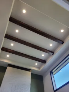 Dark stained parallel ceiling beams on a sloped section above a textured accent wall